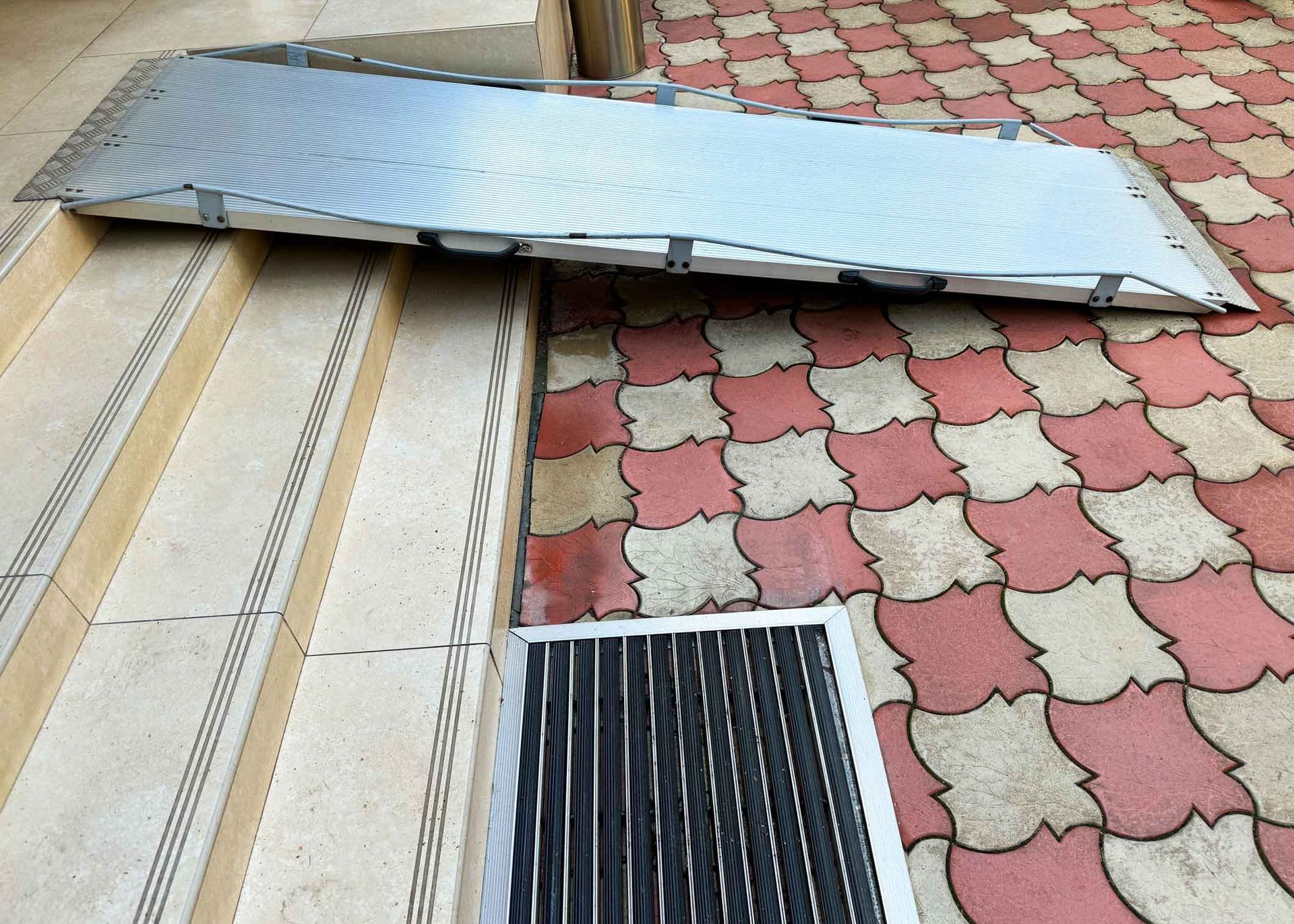 Collapsed metal awning lying over patterned sidewalk tiles and a drainage grate
