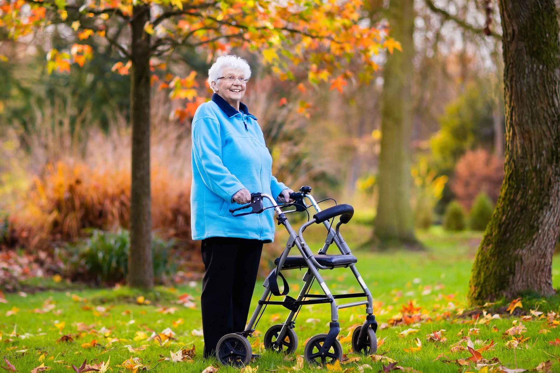 Older adult standing with a walker in a fall park with orange leaves and trees