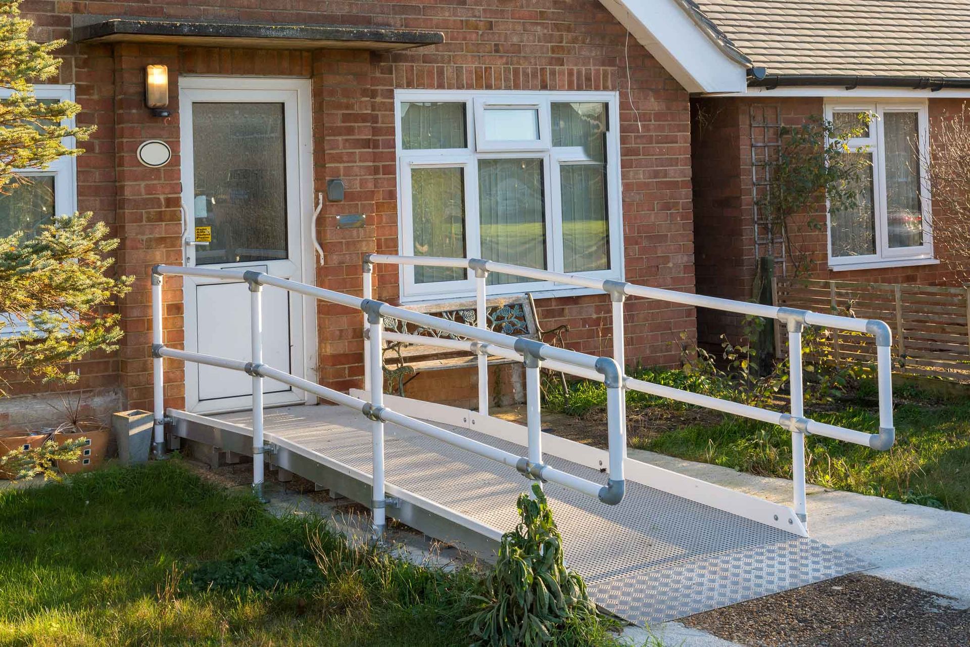 Brick building entrance with a white metal wheelchair ramp and handrails leading to a door.