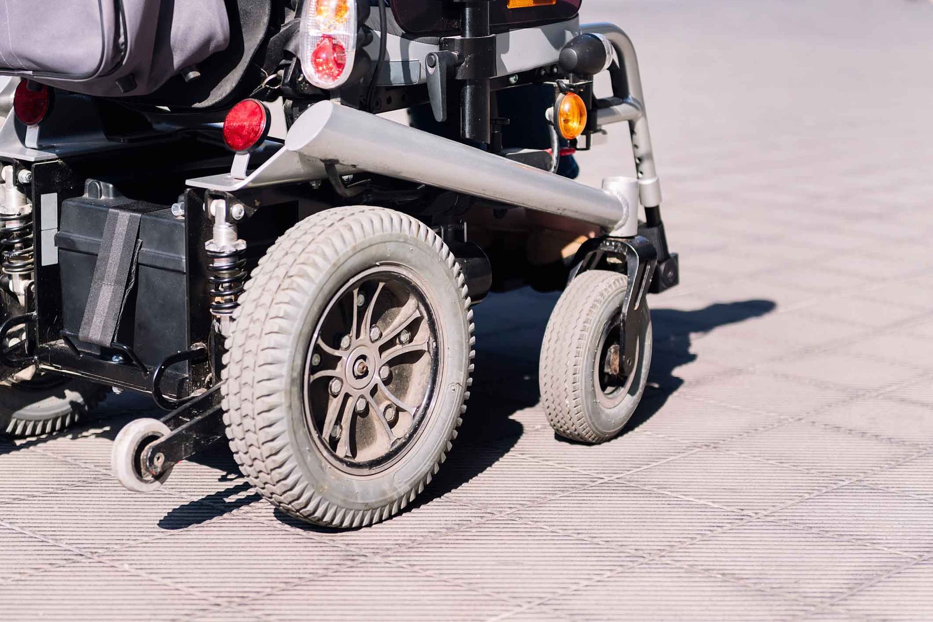 Rear view of a black mobility scooter on a paved surface, showing large rear wheels and seat cargo rack