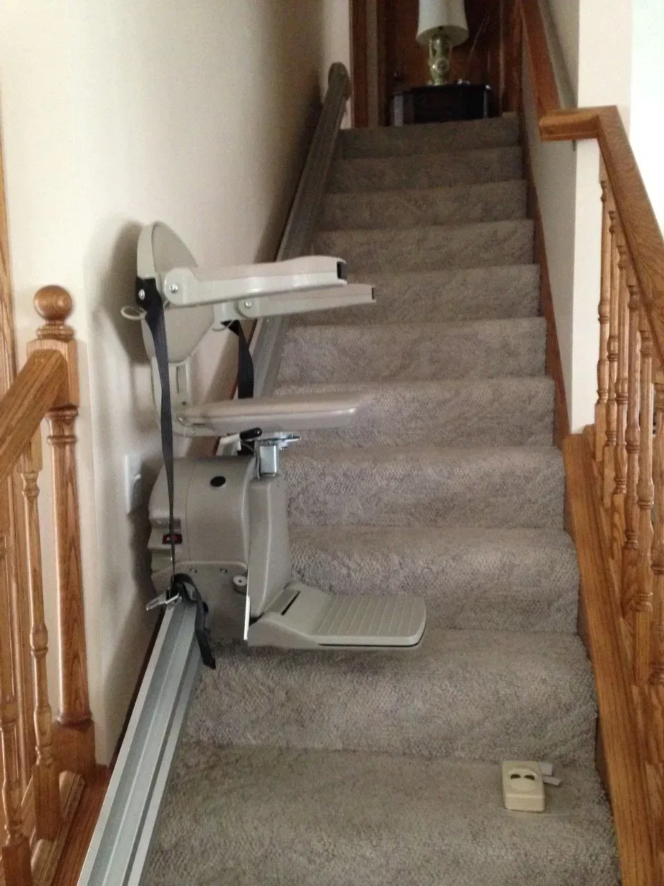 Stair lift chair installed on a carpeted indoor staircase with wooden banister rails.