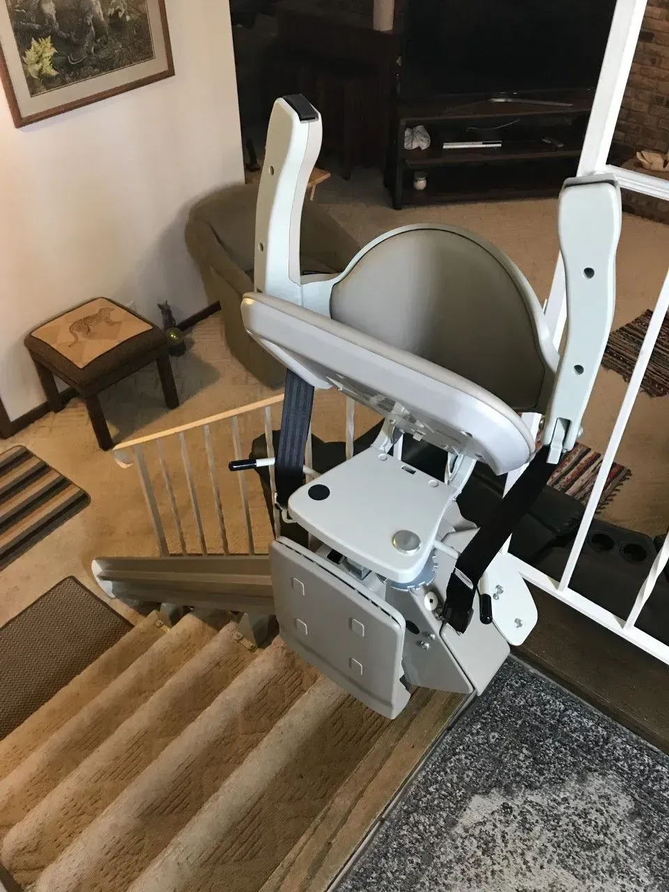 Stairlift attached to a carpeted staircase in a home interior, with the seat facing the steps.