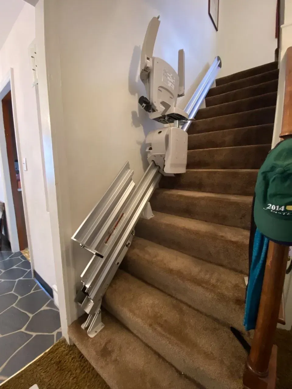 Stairlift folded beside a carpeted staircase in a home hallway, with folded rails leaning against the wall.