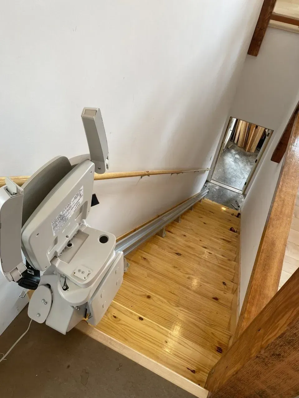 Indoor stairlift beside a narrow wooden staircase with a metal landing at the bottom.