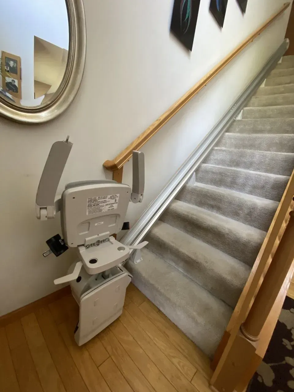 Stairlift chair at the base of a carpeted staircase with wooden handrails.