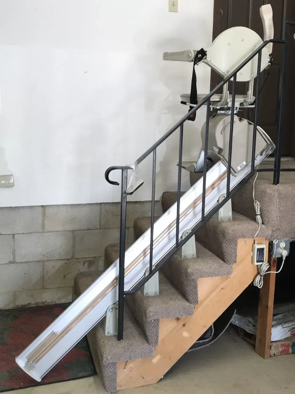 Long metal ramp propped on stairs in a building interior, with handrails and stacked chairs nearby