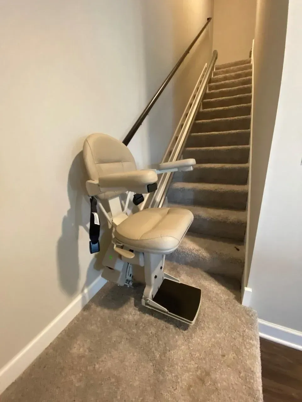 Stairlift chair at the base of a carpeted staircase in a narrow hallway