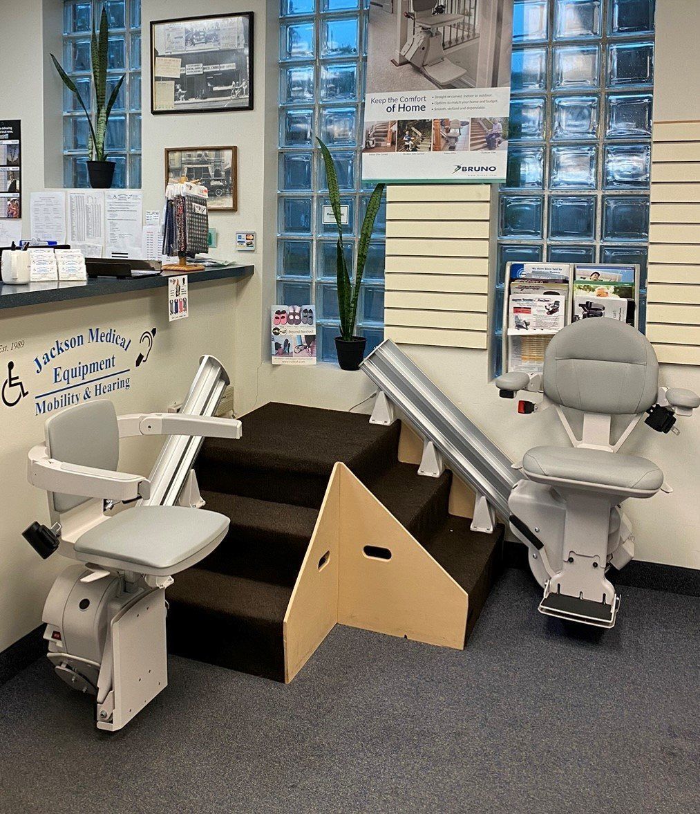 Two white pediatric wheelchairs beside a small brown ramp in a therapy room with windows and posters
