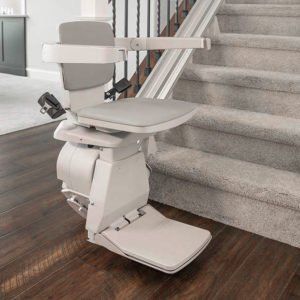 White stairlift with seat and footrest mounted beside carpeted stairs in a home interior