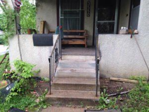 Front porch steps with black metal handrails leading to a small covered entryway
