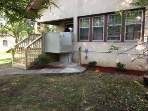 House exterior with small wooden ramp and steps leading to a side entrance, windows, and a grassy yard