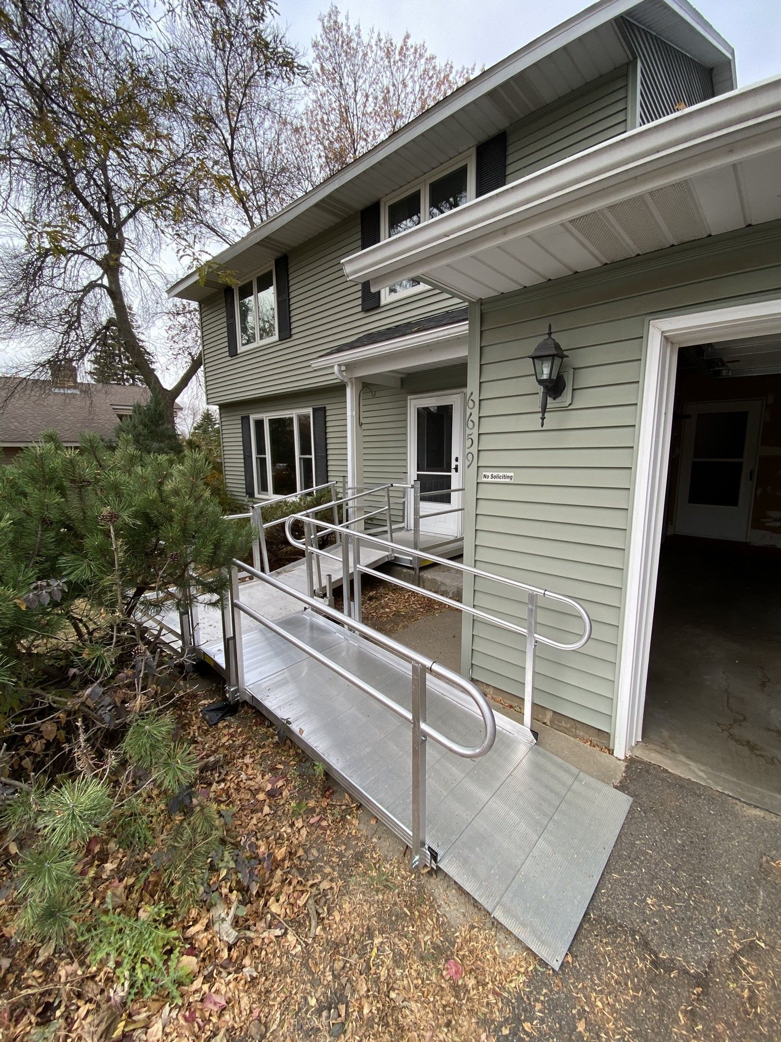 Front porch ramp with metal railings on a green house, covered entry and steps nearby