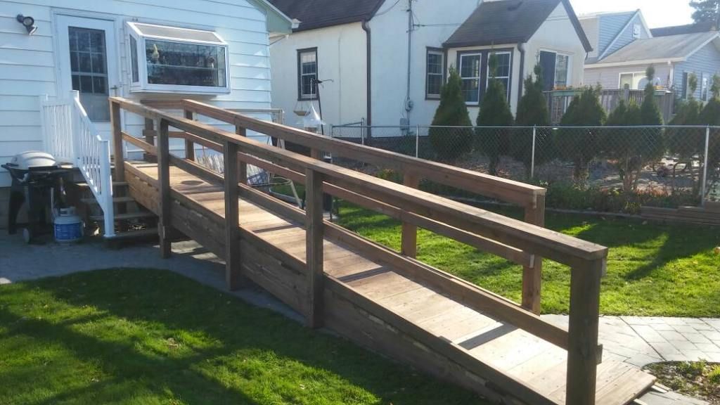 Wooden wheelchair ramp beside a white house, leading from the lawn to the side entrance.