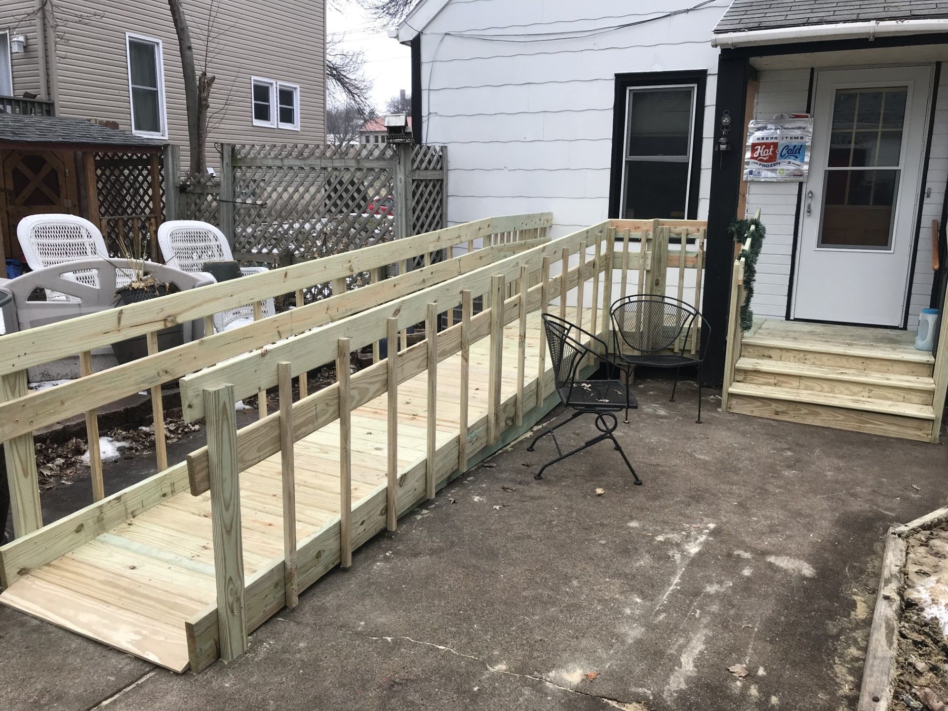 Wooden accessibility ramp leading to a house entrance with steps and a small patio area