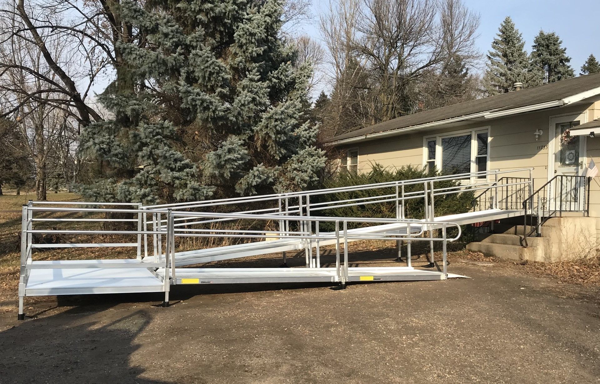 White accessibility ramp with railings leading to a beige house on a gravel driveway.