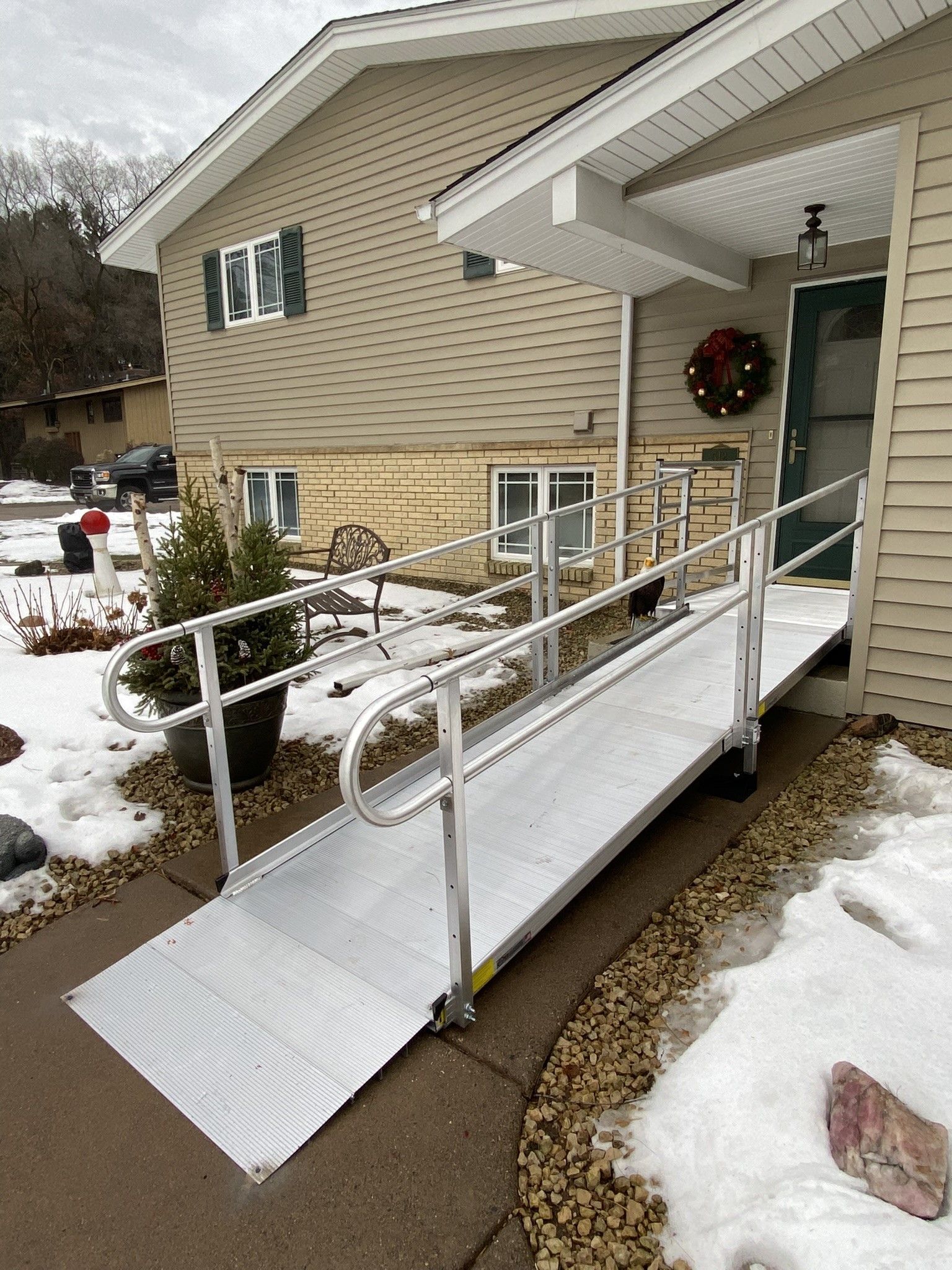 Snow-covered wheelchair ramp leading to a house entrance with white railings and green door