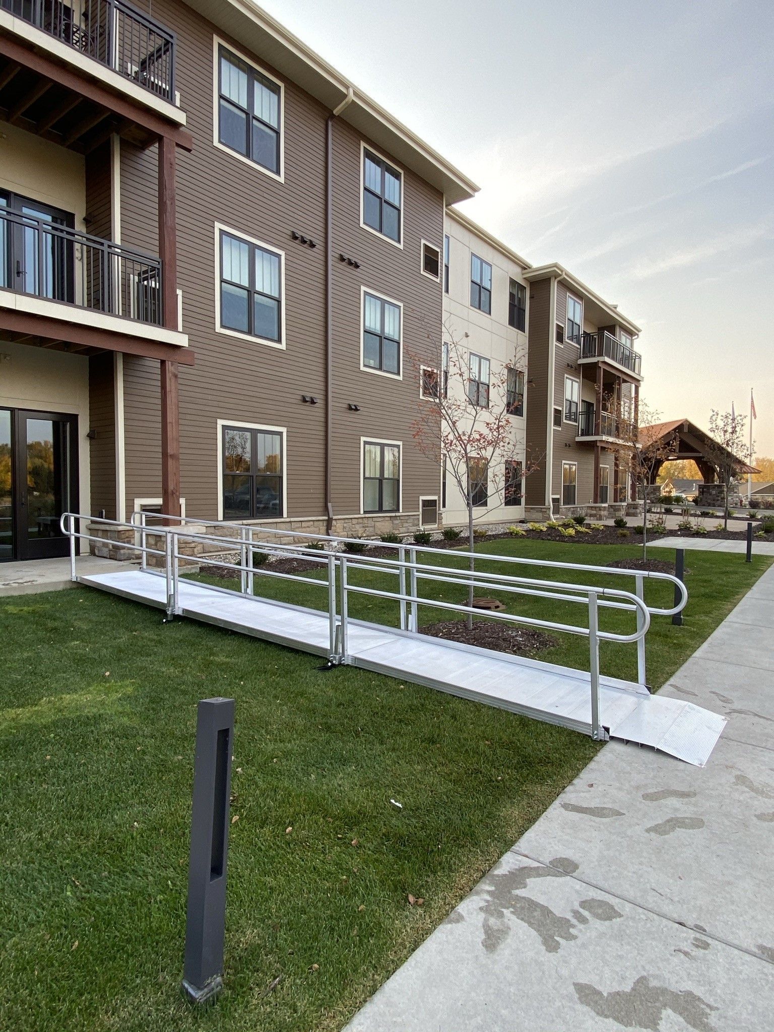 Apartment building exterior with ramped walkway, grass lawn, and balconies in a residential complex