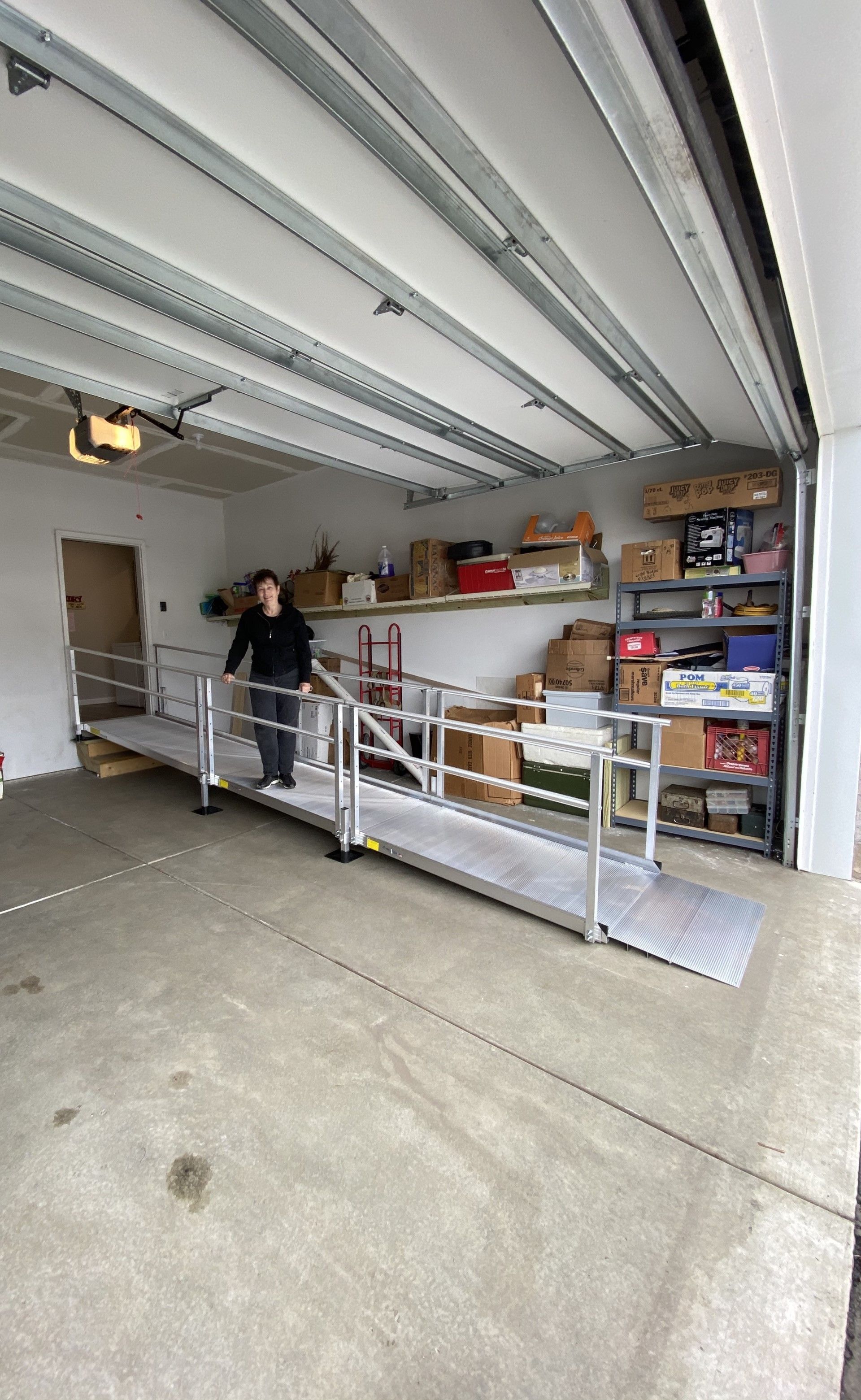Person standing in a garage beside a metal wheelchair ramp and storage shelves