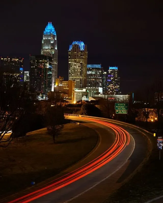 Night city skyline with glowing skyscrapers and red light trails curving along a road