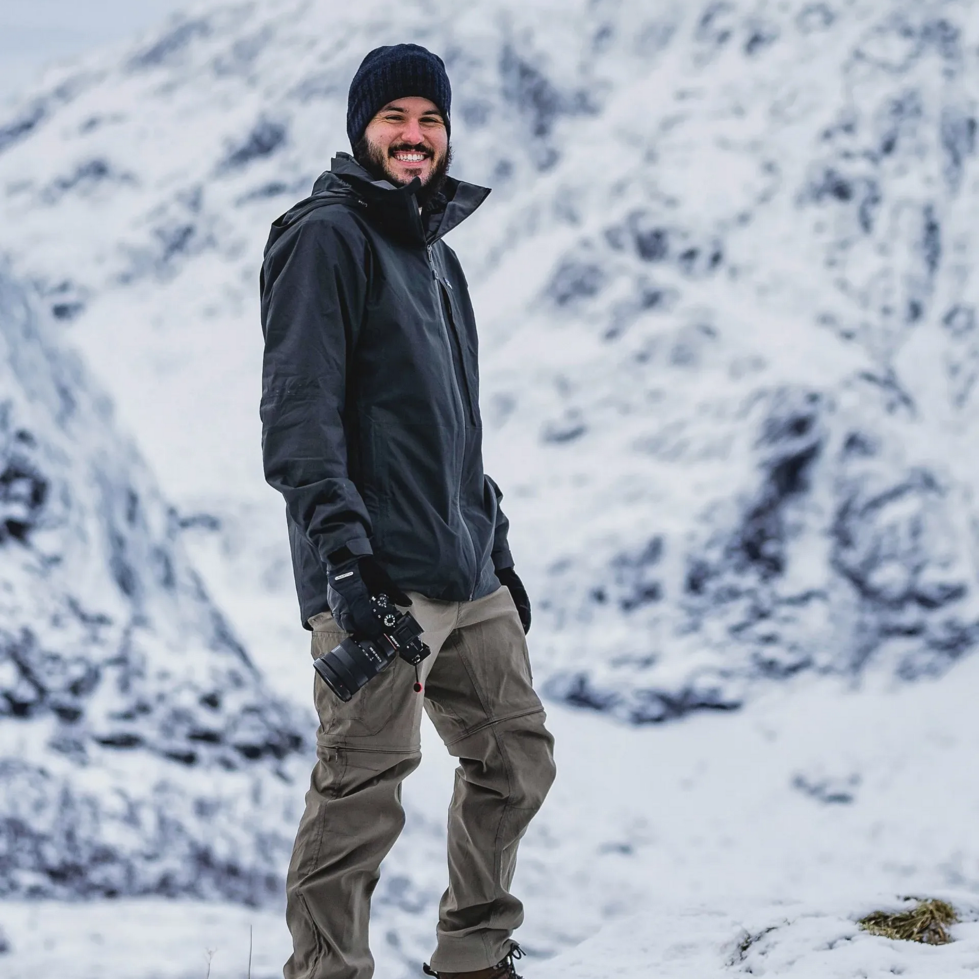Person in dark winter gear standing on snowy mountainside, smiling at the camera.