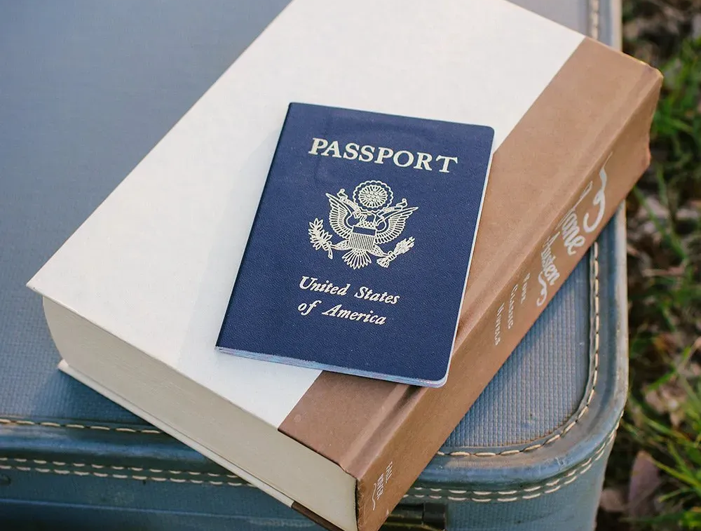 Blue U.S. passport resting on stacked books and a suitcase