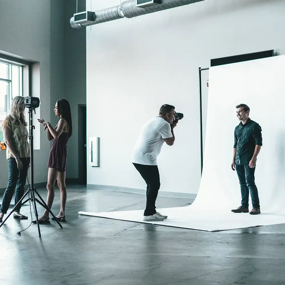 Photographer shooting a portrait in a studio with white backdrop, lights, and two assistants nearby