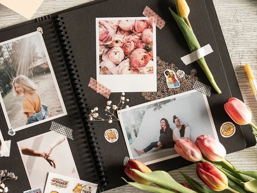Flat lay of a scrapbook with taped photos, tulips, and decorative stickers on a textured gray surface
