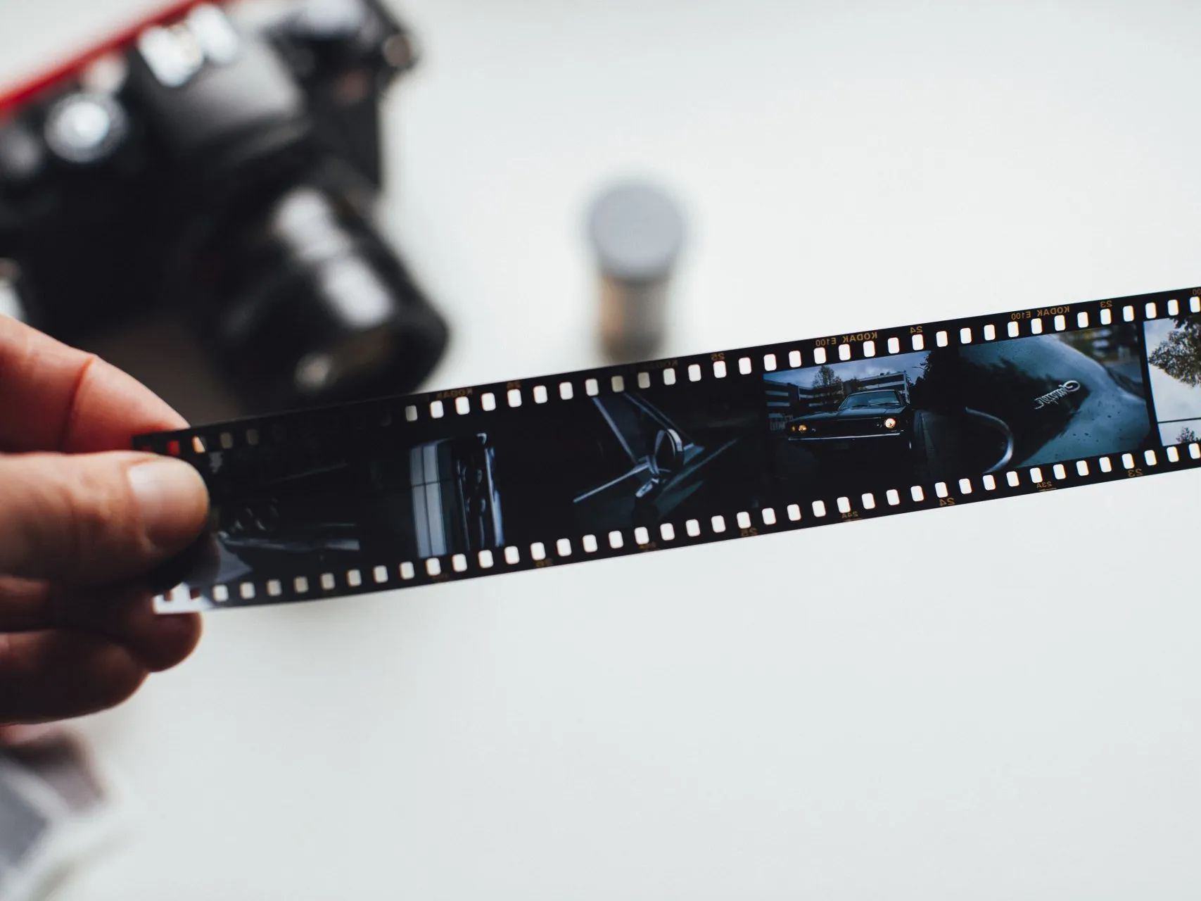 Hand holding a 35mm film strip with photos, with a blurred camera in the background