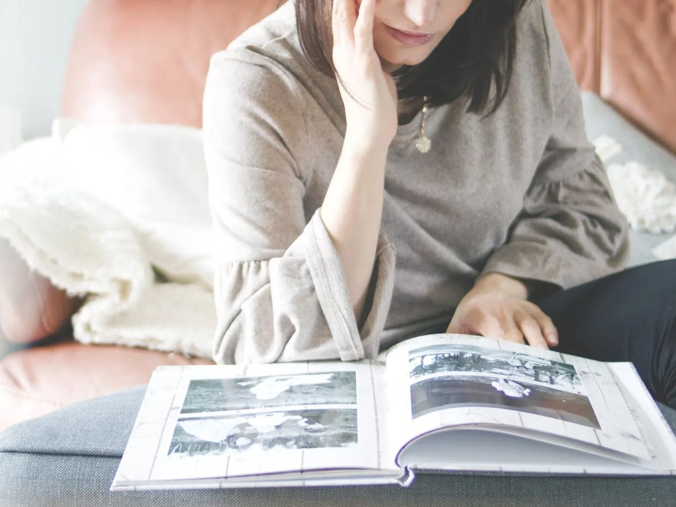 Person sitting on a bed, reading an open book with black-and-white photos.