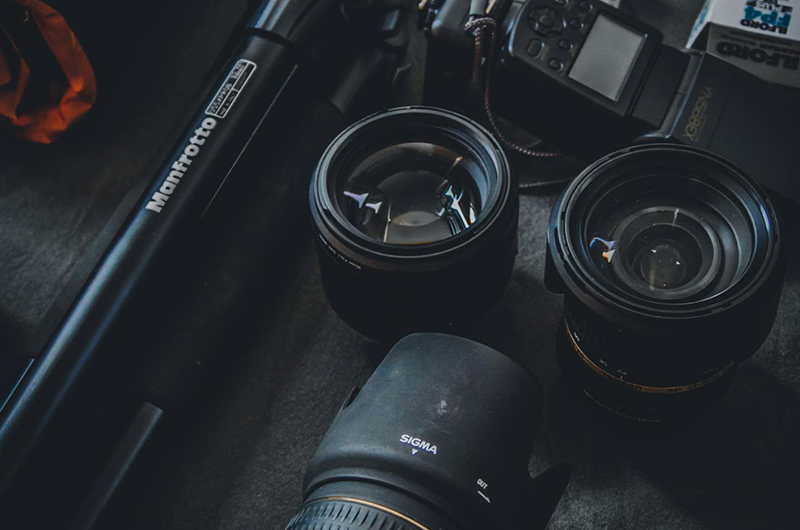 Camera lenses and accessories arranged on a dark tabletop under moody lighting