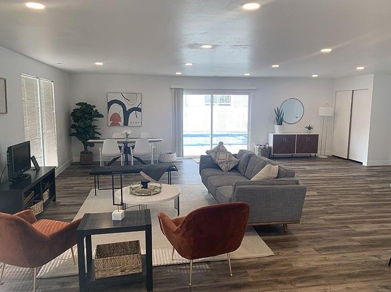 Spacious modern living room with gray sofa, red chair, coffee table, fireplace, and large window at Creekside Village apartments in Sandy, UT.