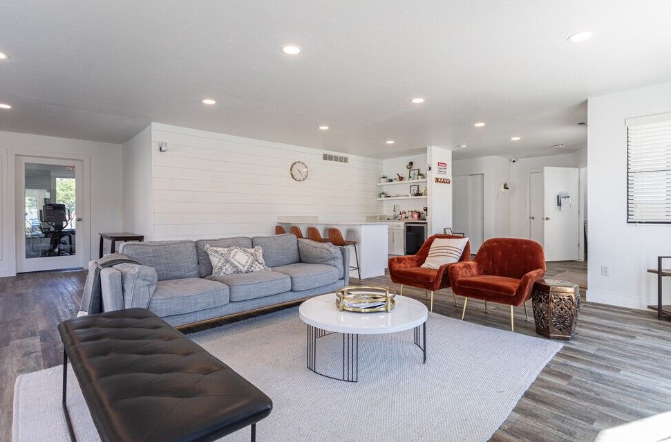 Bright modern living room with gray sectional, red chairs, round coffee table, and light wood floors at Creekside Village apartments in Sandy, UT.