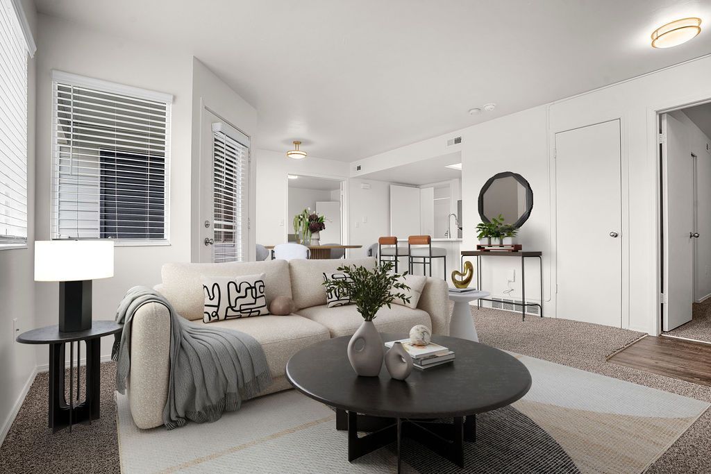 Bright modern living room with a gray sofa, round black coffee table, lamp, and large windows at Creekside Village apartments in Sandy, UT.