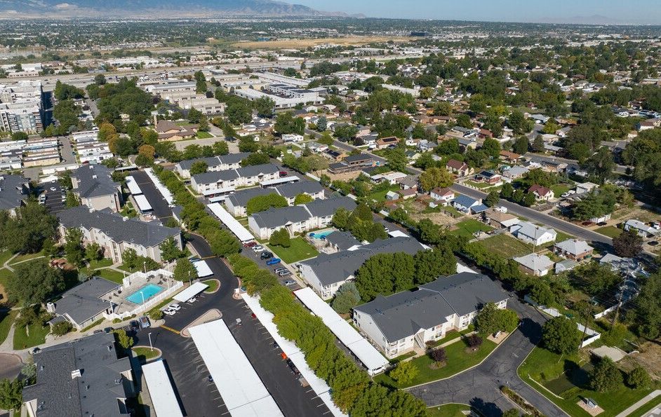 Aerial view of a suburban neighborhood with houses, trees, streets, and distant cityscape under a clear sky at Creekside Village apartments in Sandy, UT.