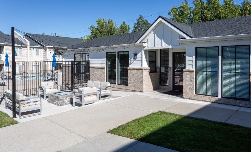 Modern patio with outdoor seating, sliding glass doors, and a small lawn beside a house at Creekside Village apartments in Sandy, UT.