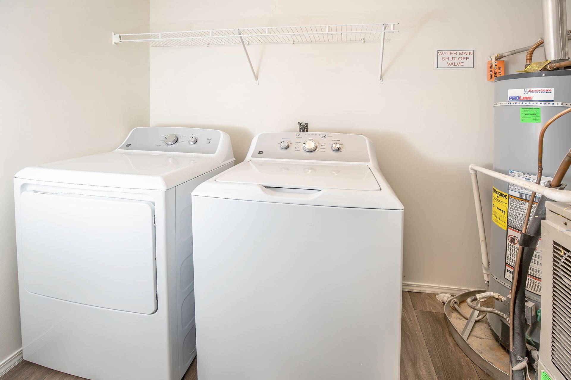 Two white washing machines in a laundry room with shelves and utility items nearby.