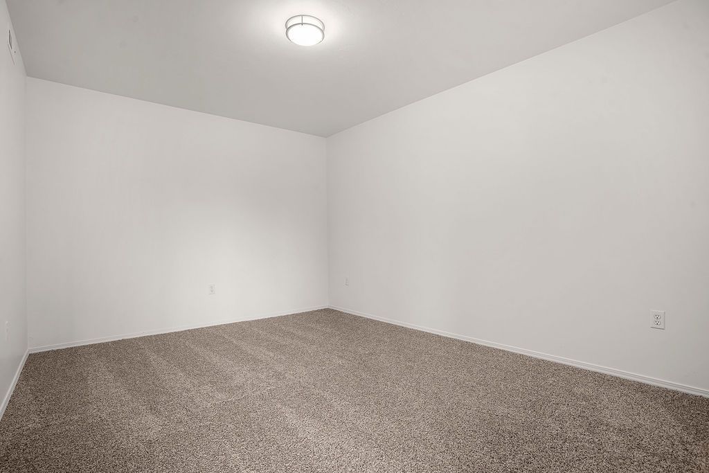 Empty white carpeted room with plain walls and a ceiling light fixture at Creekside Village apartments in Sandy, UT.