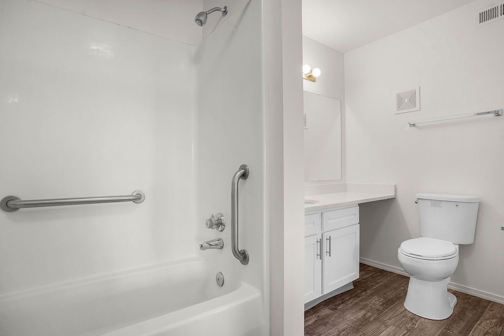 Accessible bathroom with tub, grab bars, sink, and toilet on wood-look flooring at Creekside Village apartments in Sandy, UT.