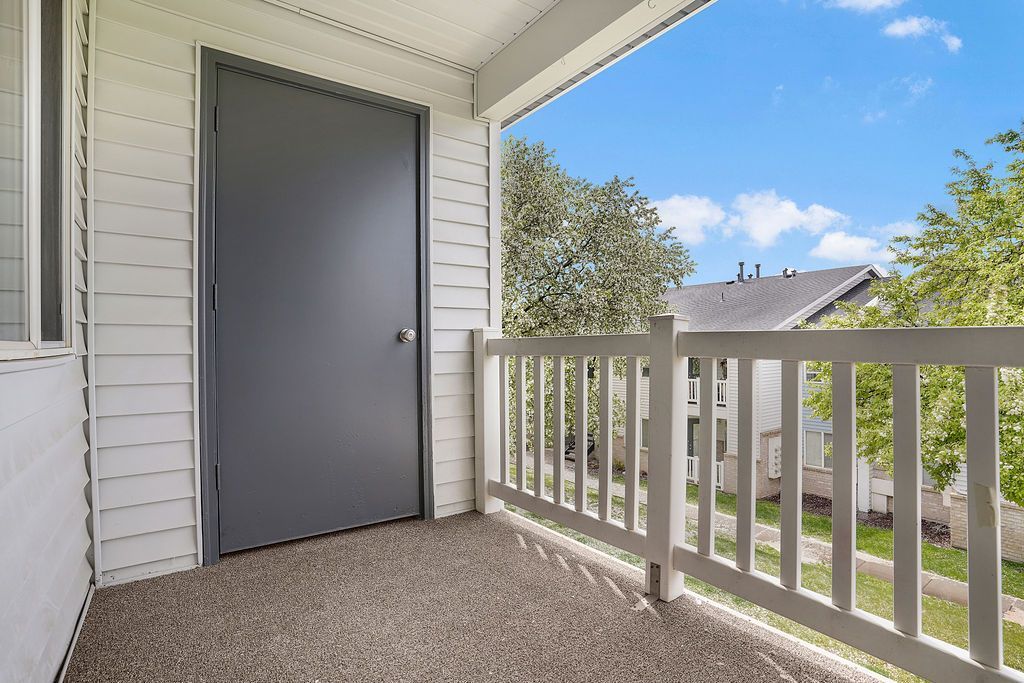 Apartment balcony with gray door, white railing, and a view of trees and neighboring homes at Creekside Village apartments in Sandy, UT.