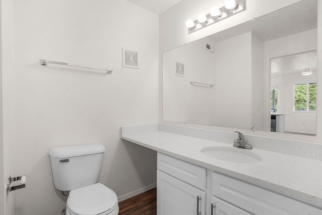 Bright bathroom vanity with mirror, white cabinets, sink, toilet, and wood floor at Creekside Village apartments in Sandy, UT.