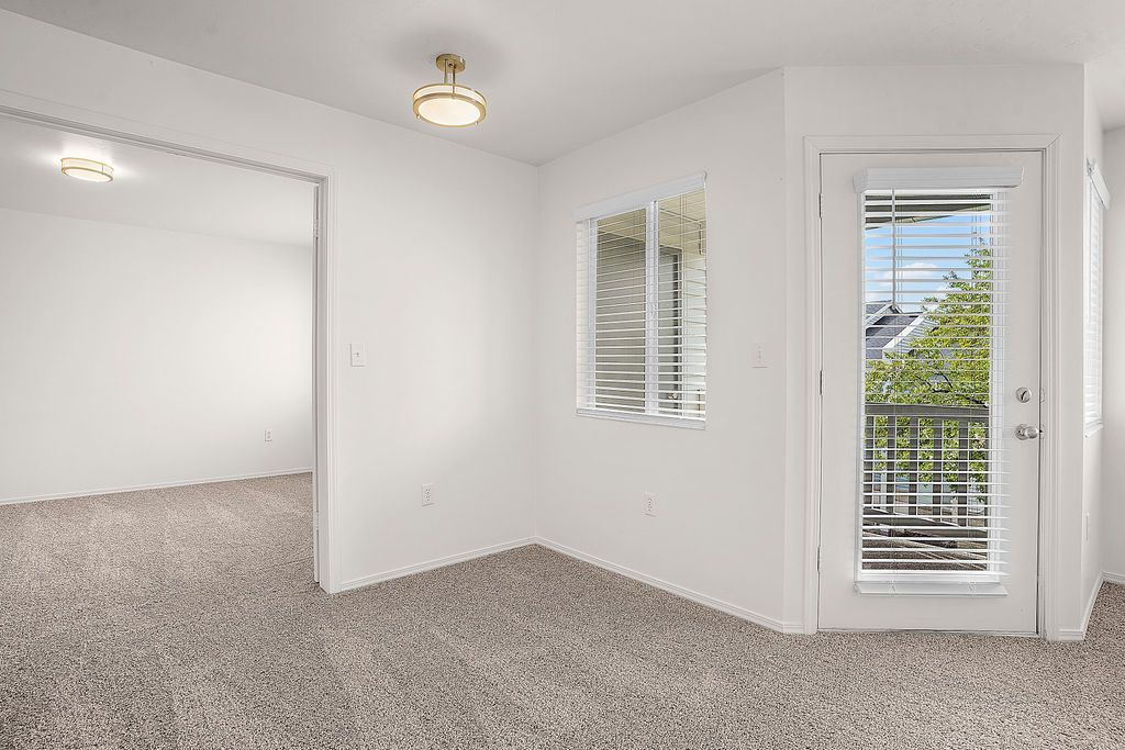 Empty white carpeted room with two windows, a glass door, and ceiling lights at Creekside Village apartments in Sandy, UT.