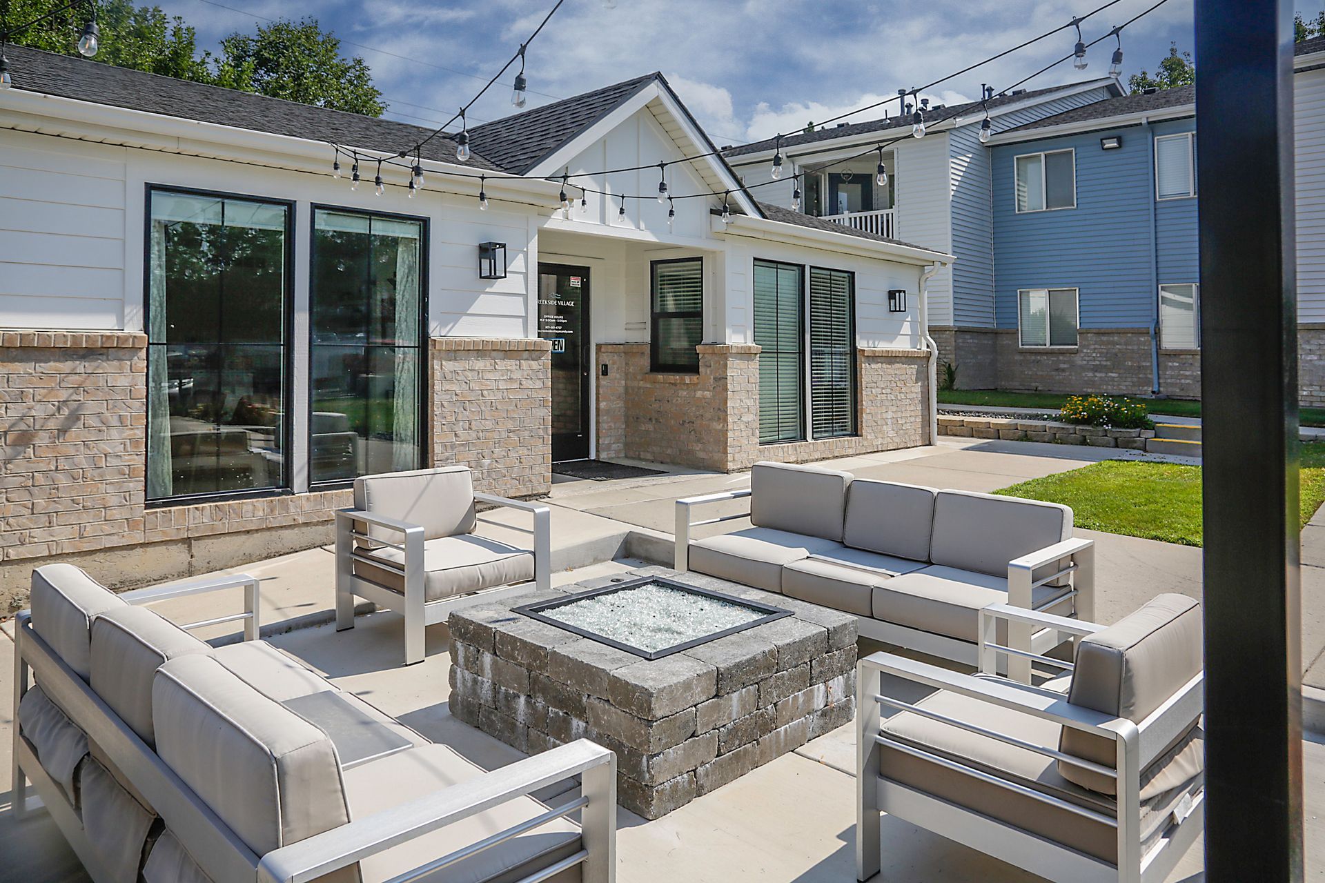 Patio with gray outdoor sofas and a stone fire pit in front of a modern house.