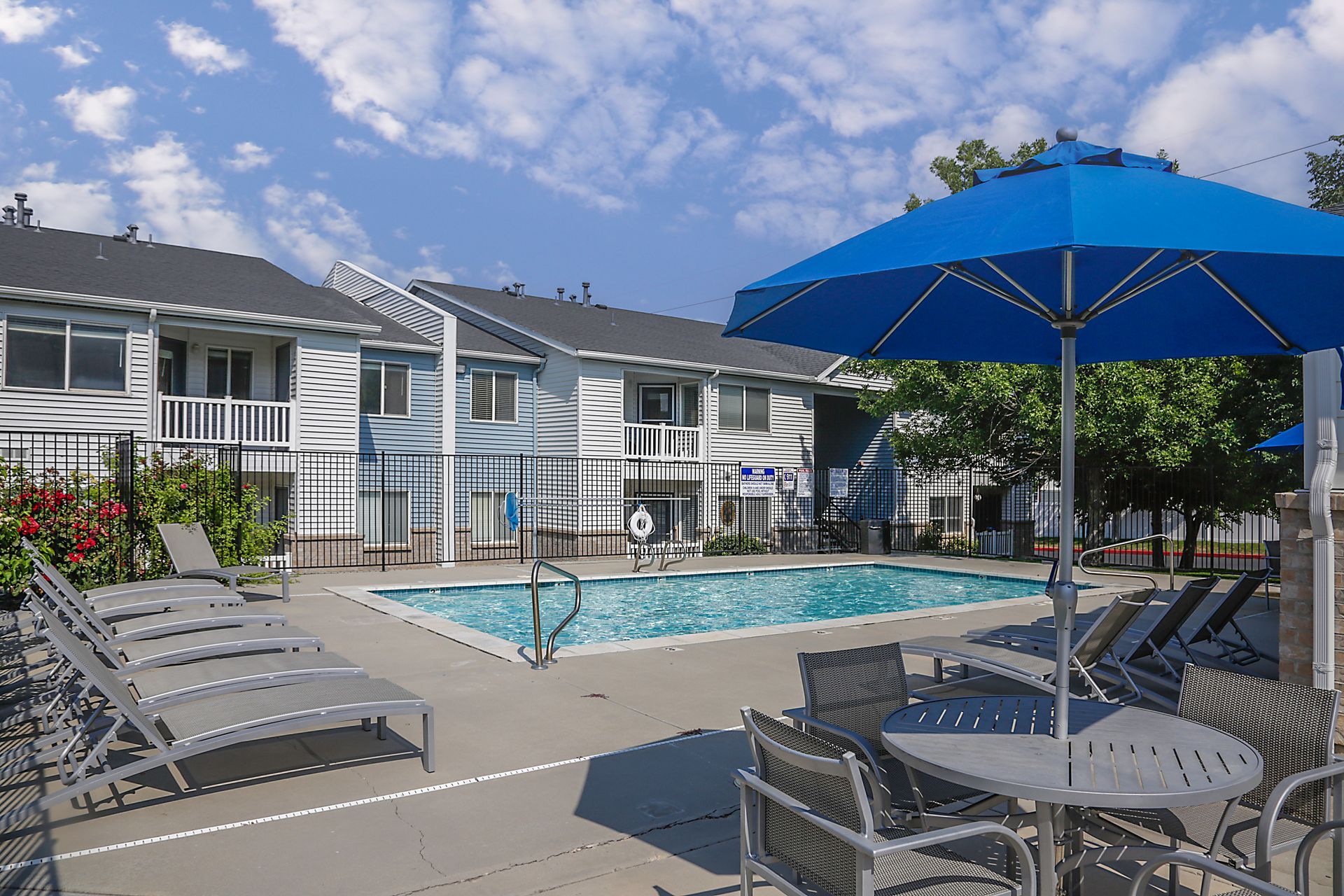 Apartment pool with lounge chairs and blue umbrellas on a sunny day
