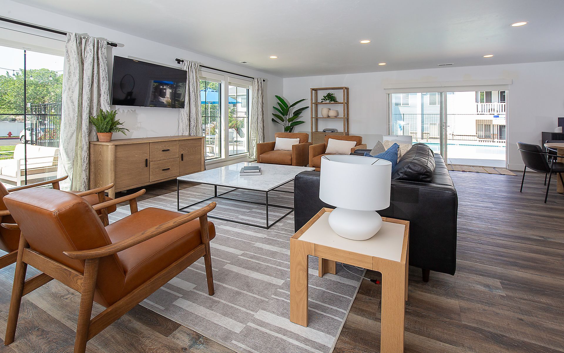 Bright modern living room with leather chairs, sofa, TV, large windows, and patterned rug.