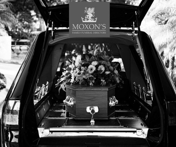 Open car hearse with floral casket arrangement and Moxon’s sign above
