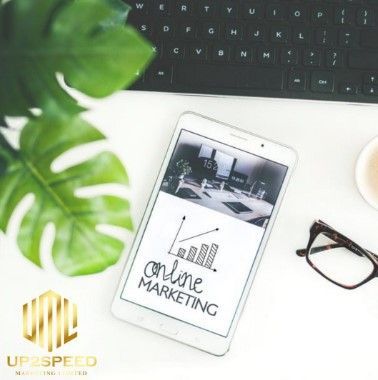Desk with tablet showing “online marketing,” keyboard, glasses, coffee cup, and green plant.