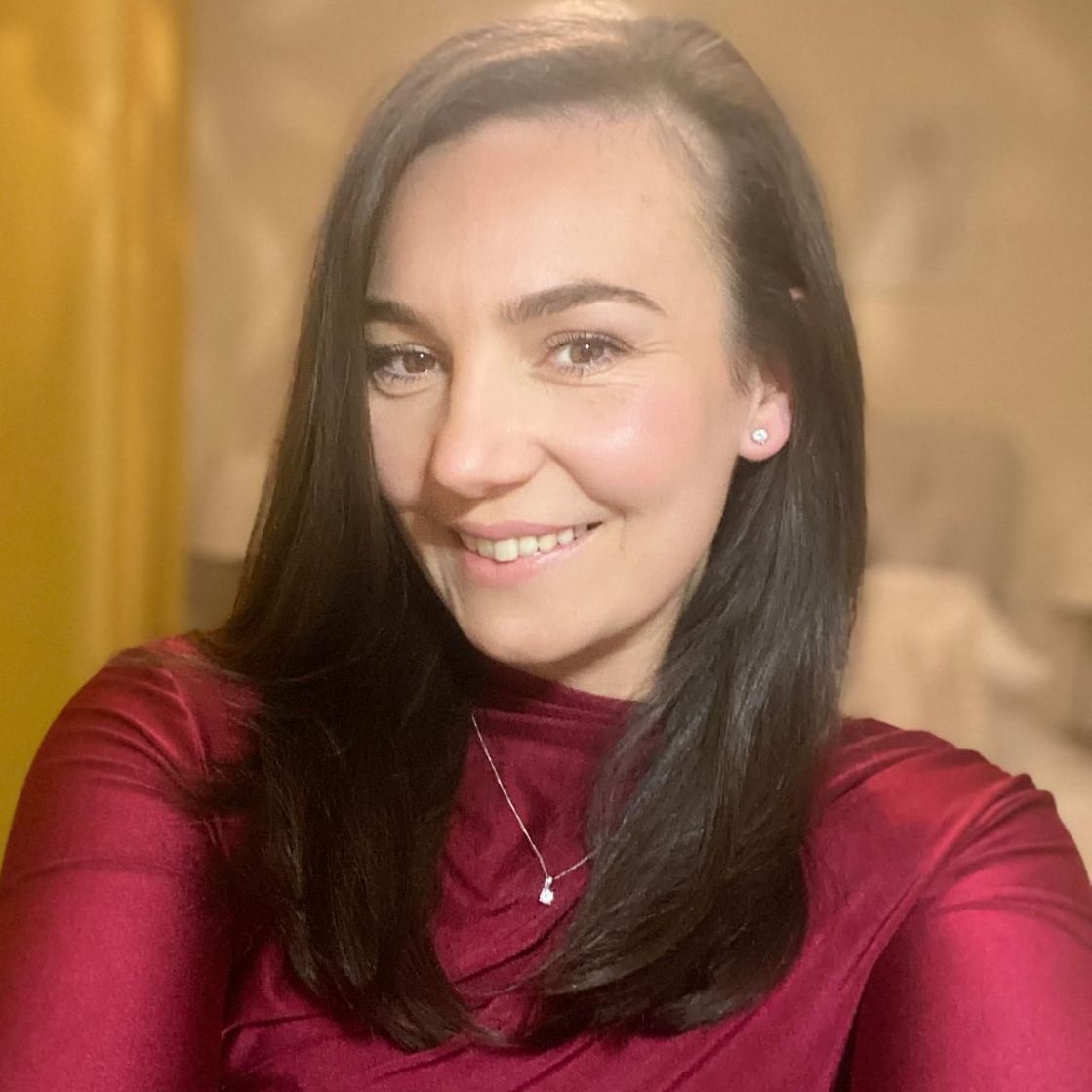 Smiling woman in a red top with long dark hair against a warm beige background