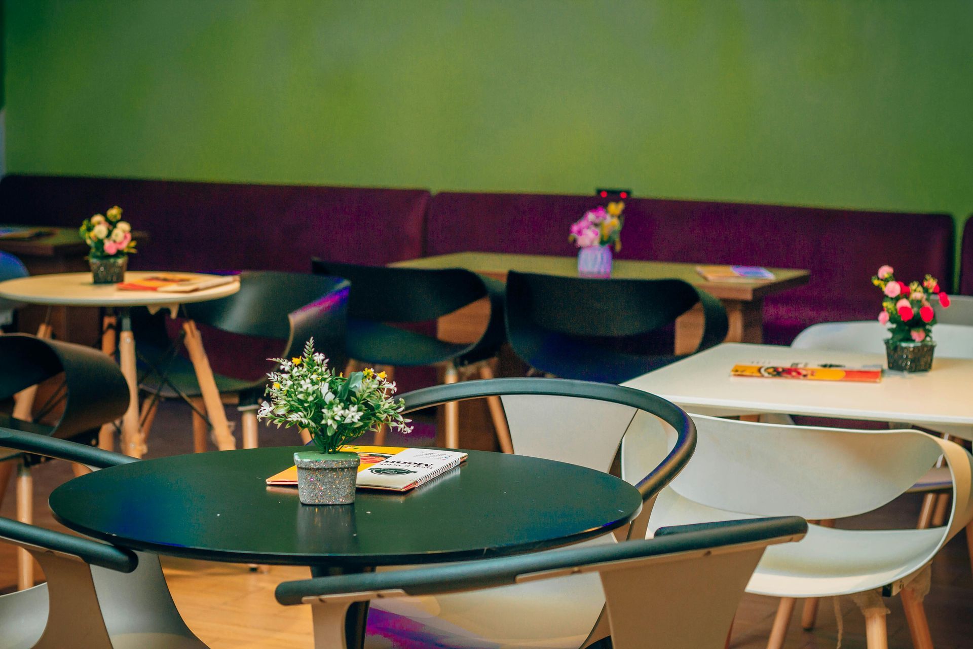 Small tables and black or white chairs are arranged in front of a purple banquette against a green wall.