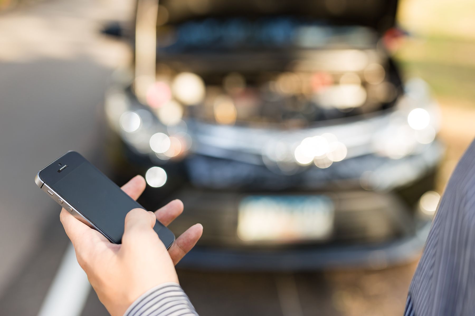 A Person Is Holding A Cell Phone In Front Of A Broken Down Car — Fase Automotive In Sunset, QLD