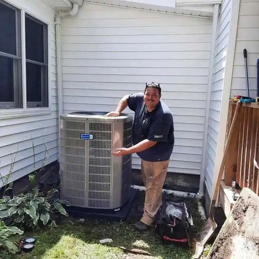 Man points at an AC unit outside a house. He wears a dark shirt and khaki pants.